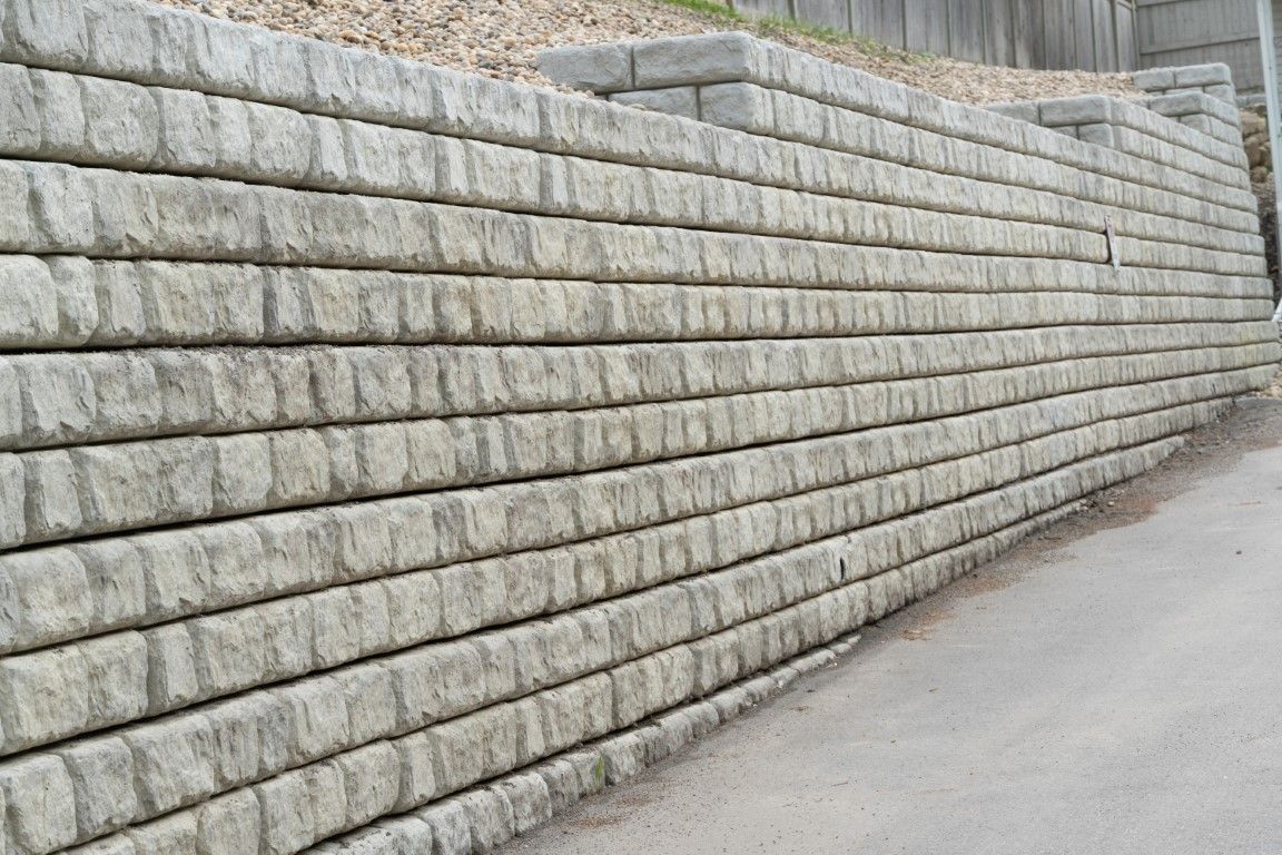 Gray concrete retaining wall alongside a road, holding back a hillside.