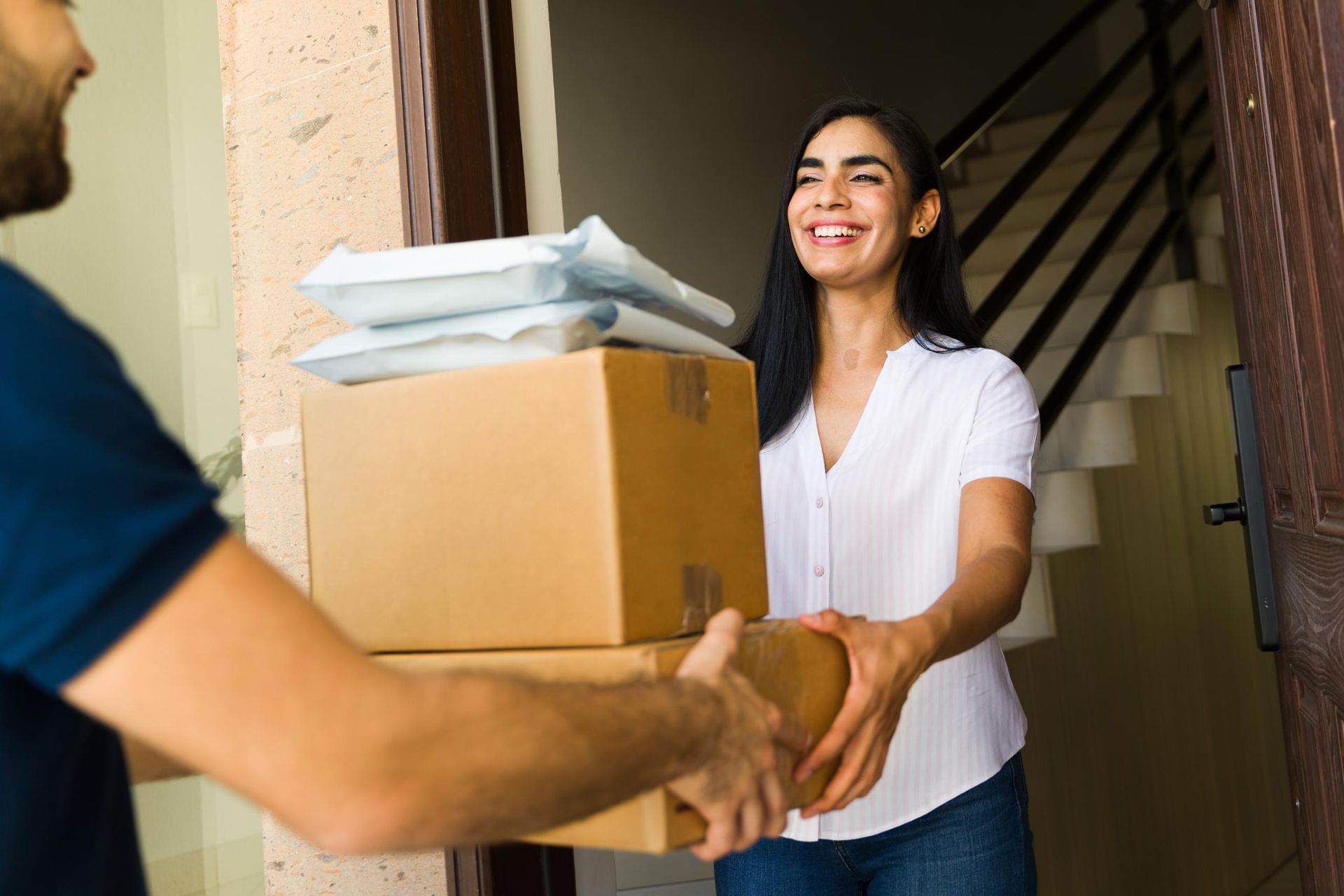 A delivery person handing packages to a smiling woman at a doorway.