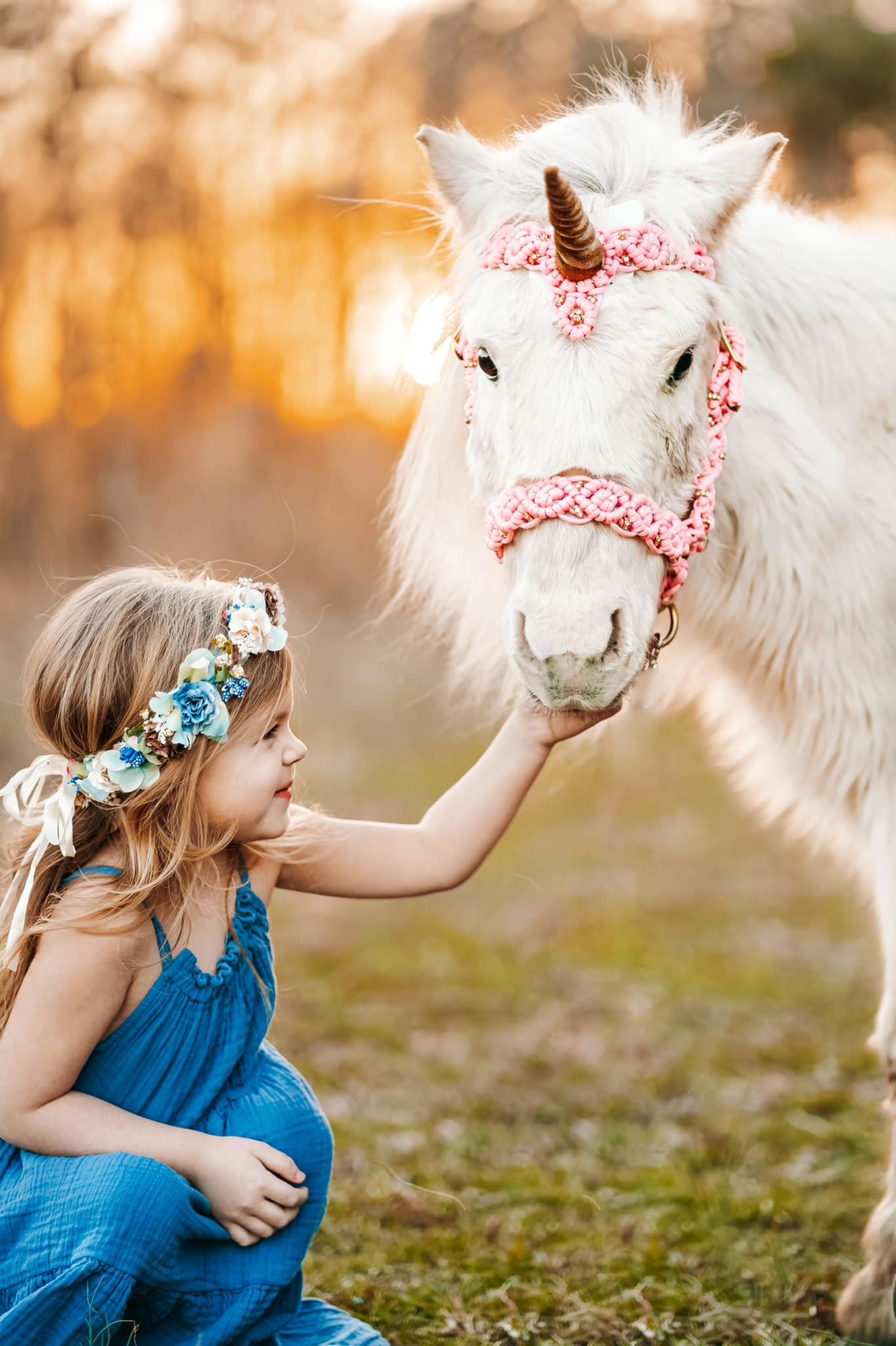 A young girl pets a white horse dressed to look like a unicorn