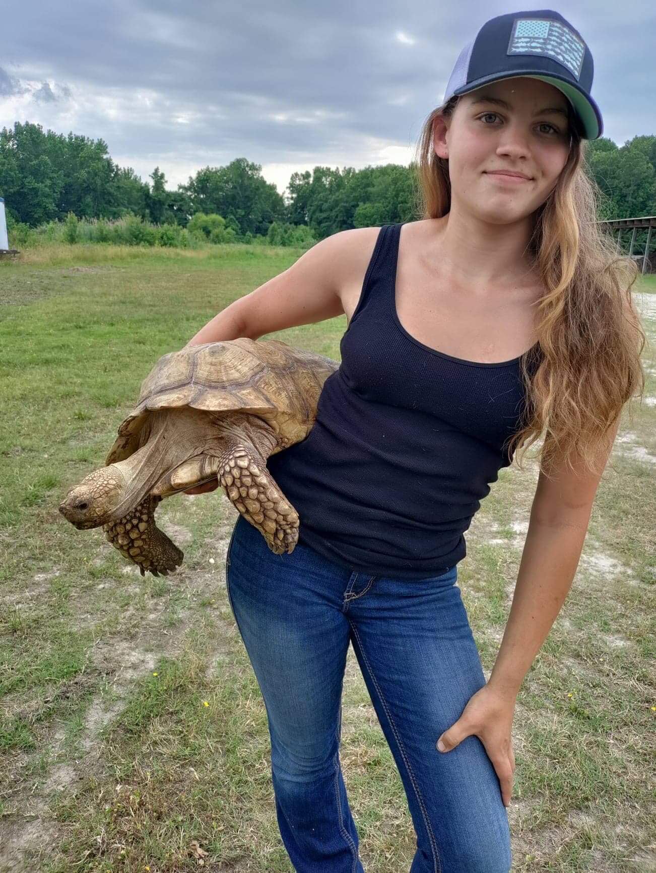 A young woman poses for the camera holding a large tortoise