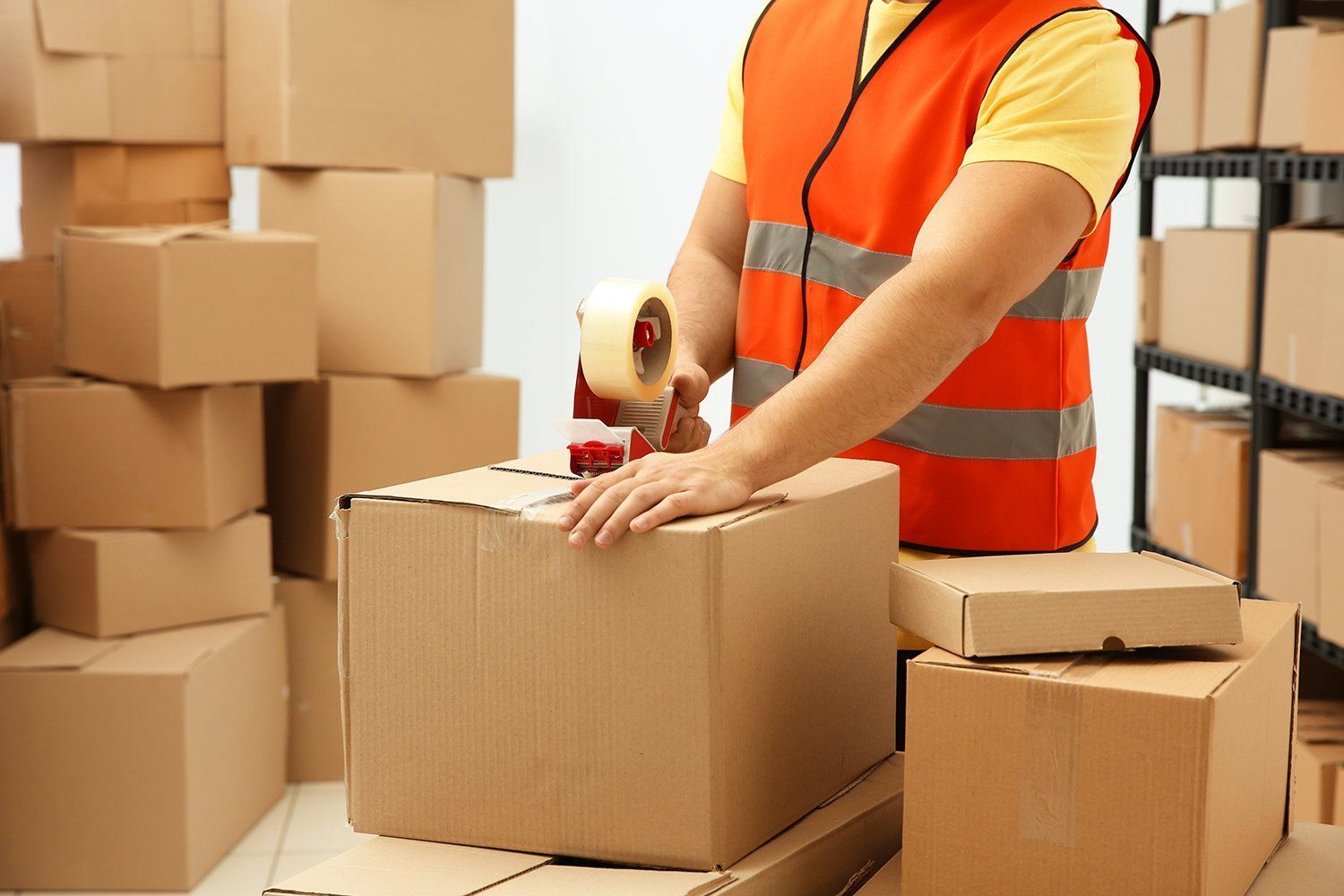 Person in Safety Vest Sealing Cardboard Box With Tape — JR Removals Mackay in Bucasia, QLD