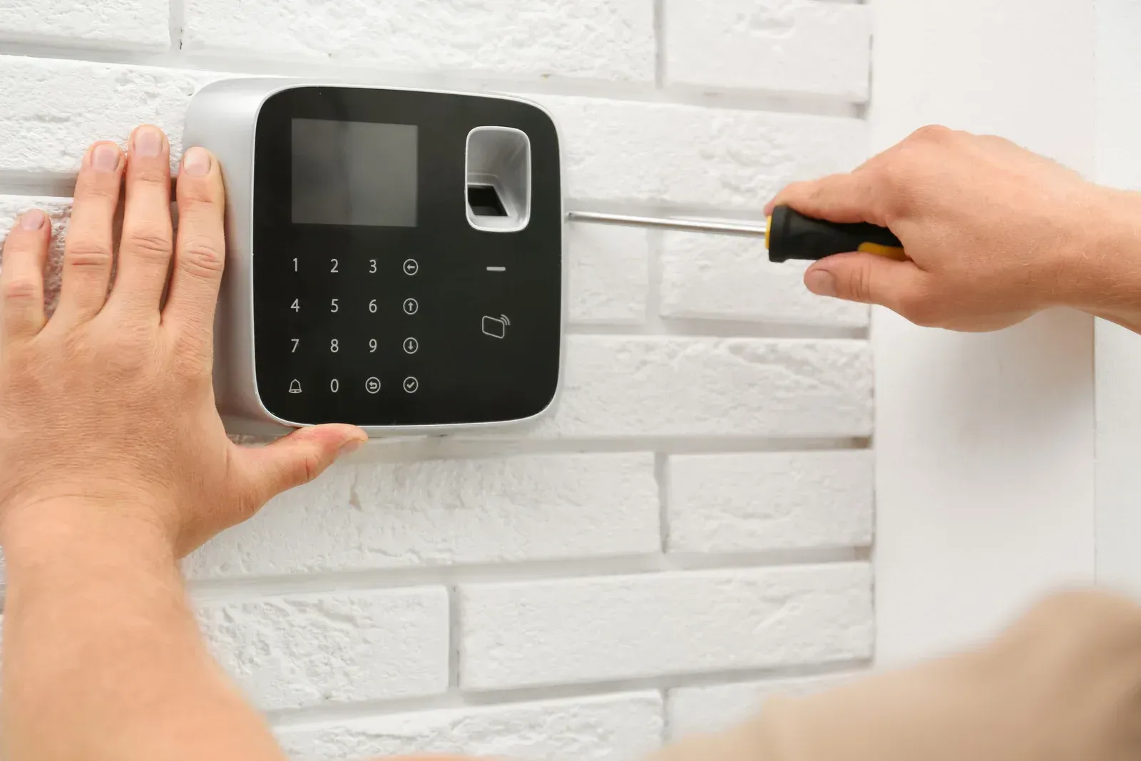 A person is installing a security system on a brick wall.