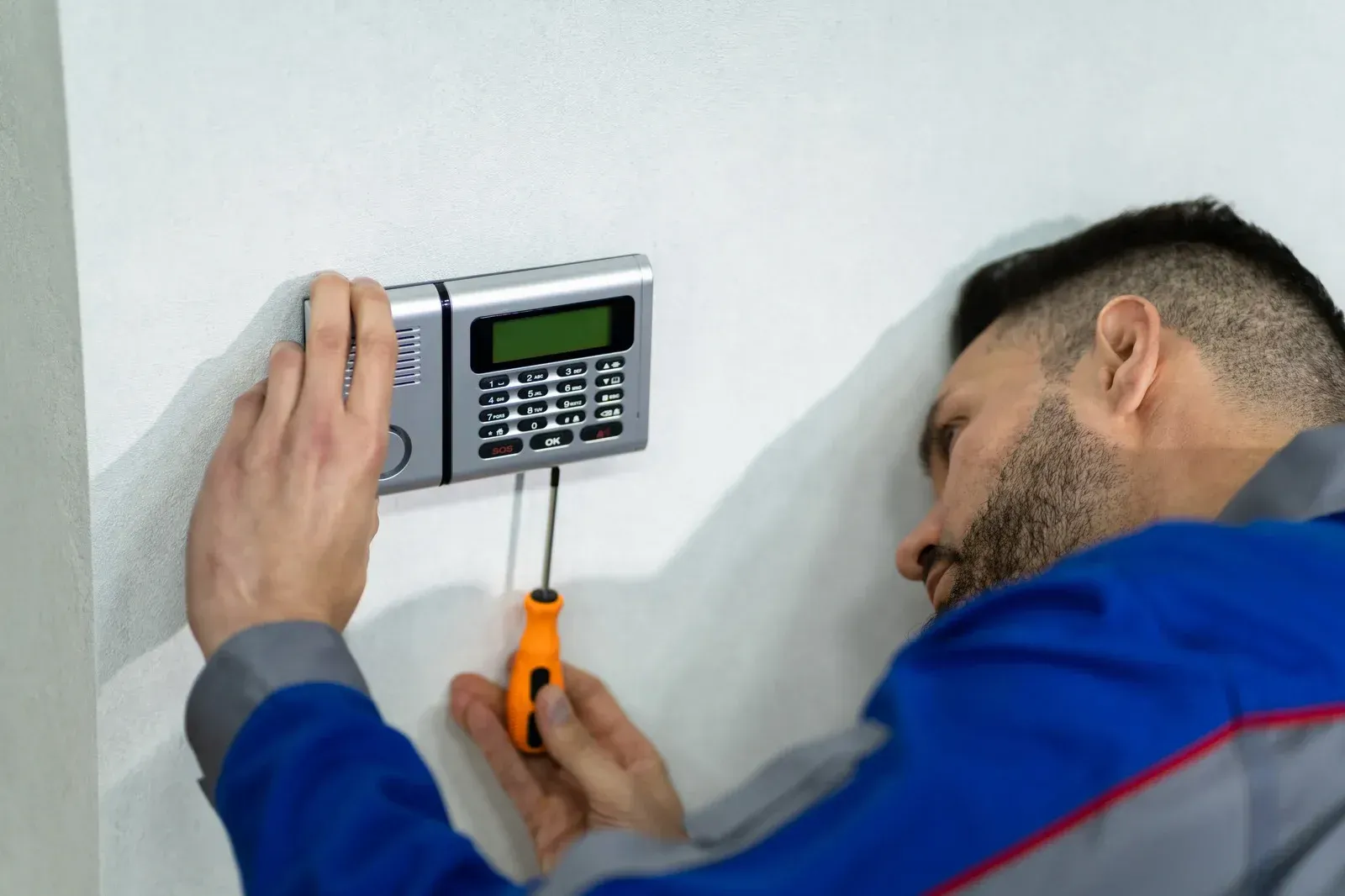 A man is installing a security system on a wall.