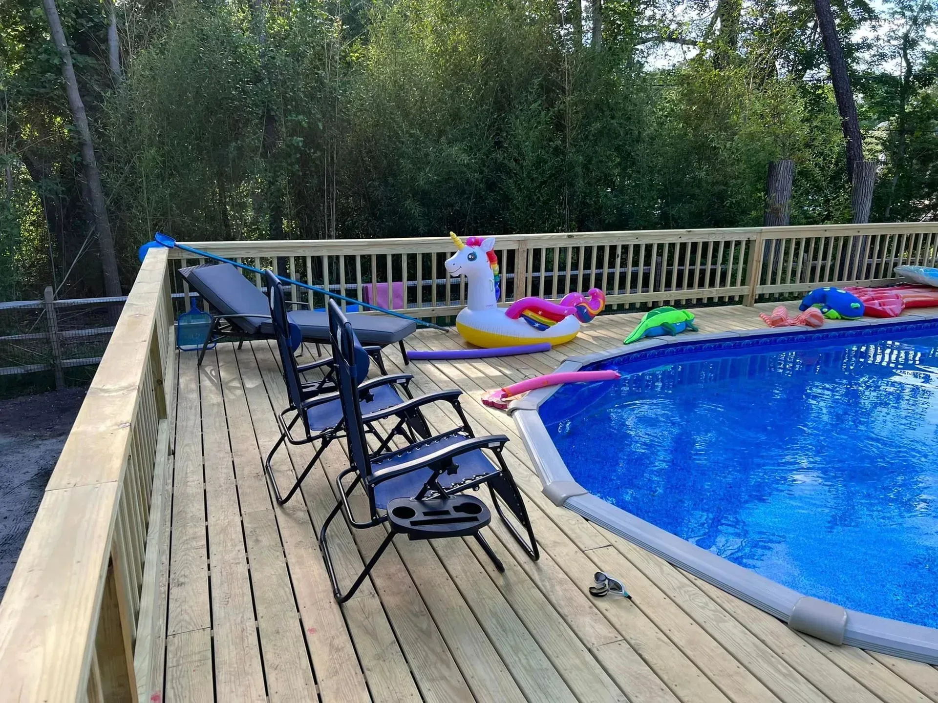Deck with blue pool, lawn chairs, and inflatable unicorn. Trees in background.
