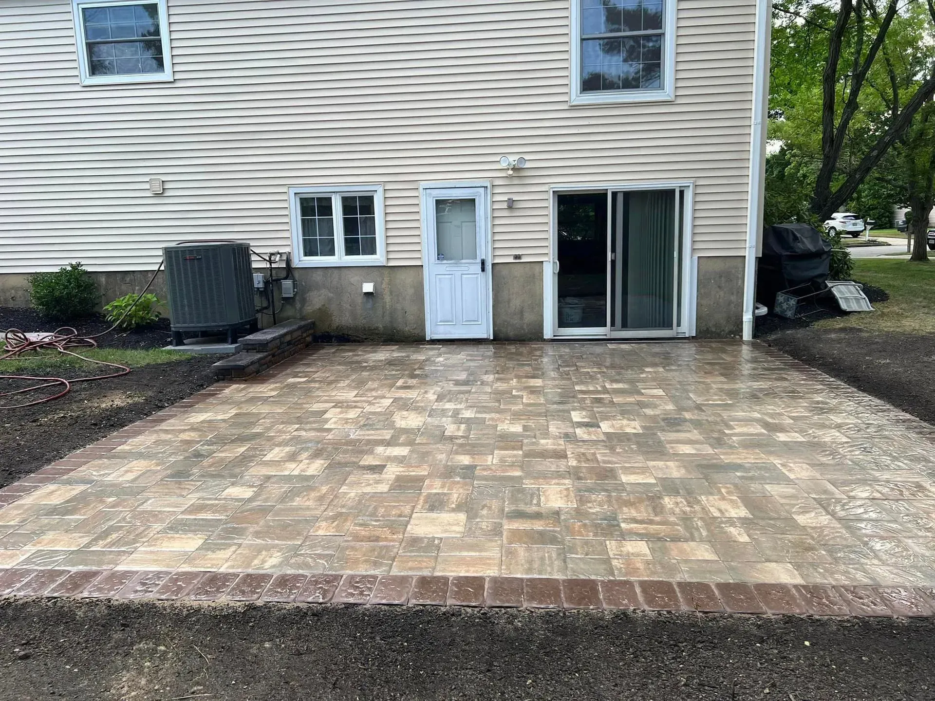 Brick patio in front of a house, door, sliding glass door, and AC unit.