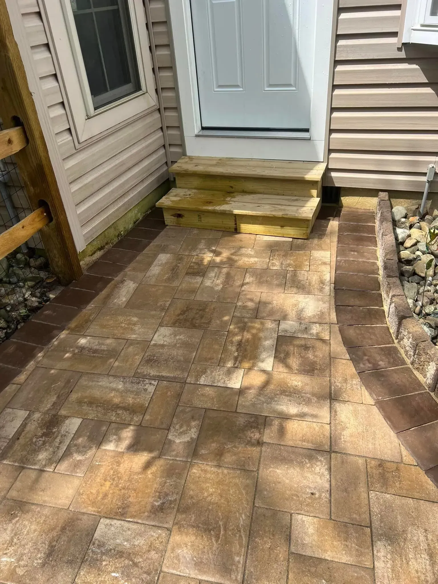 Brick walkway leads to steps and a white door of a beige house.