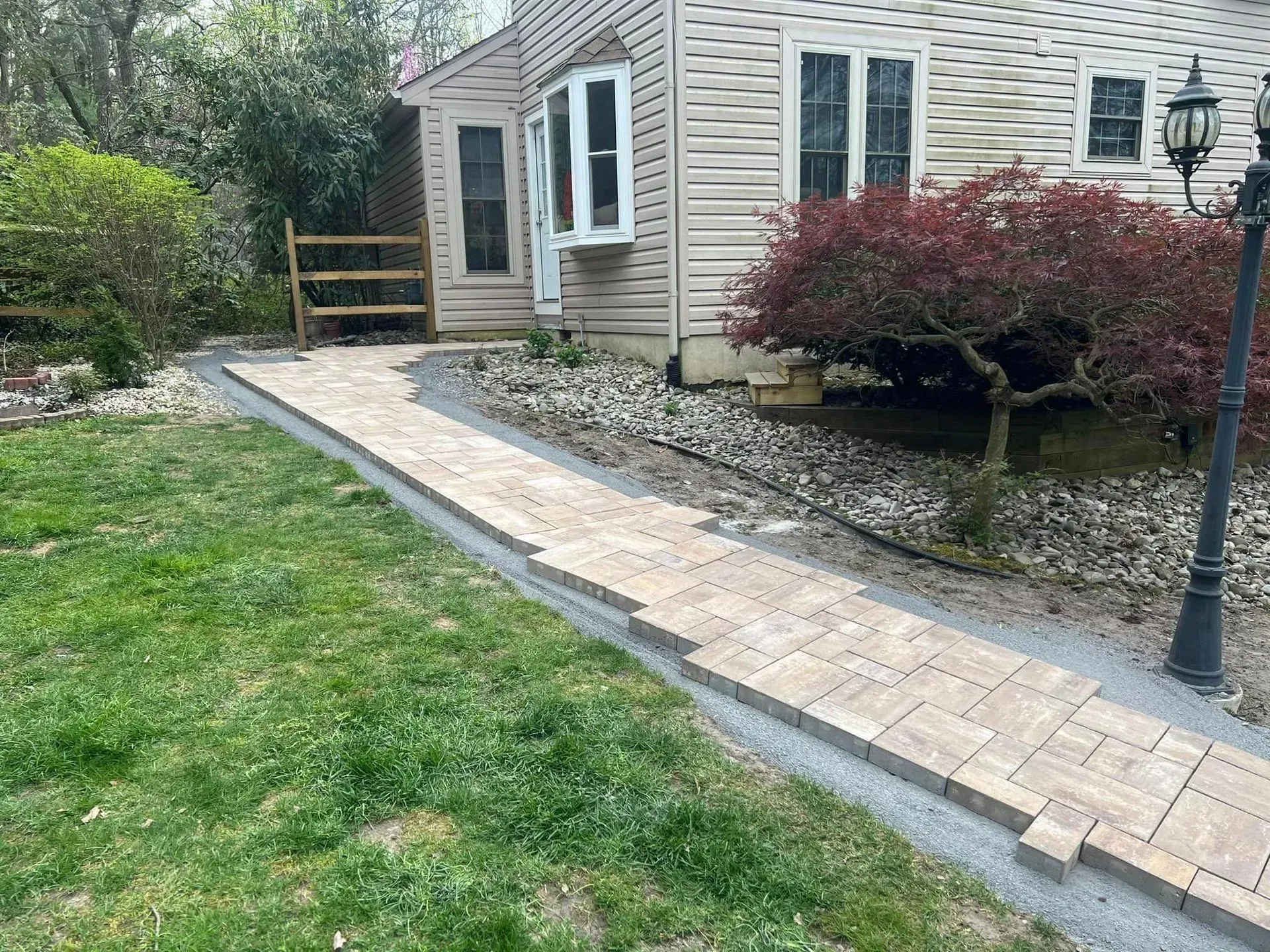 Brick walkway leading to a house with a bay window, grass and landscaping.