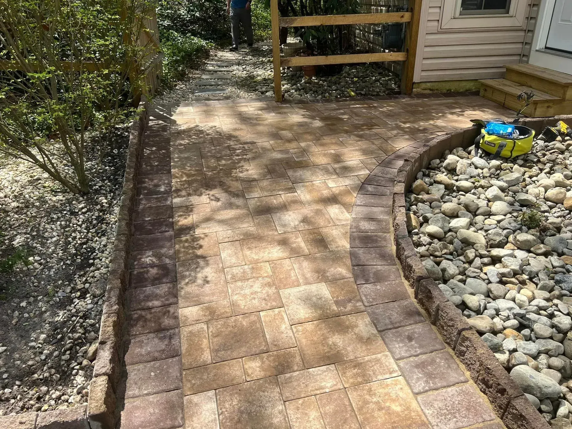 Brick pathway curves past a rock garden and small wooden fence; exterior setting.