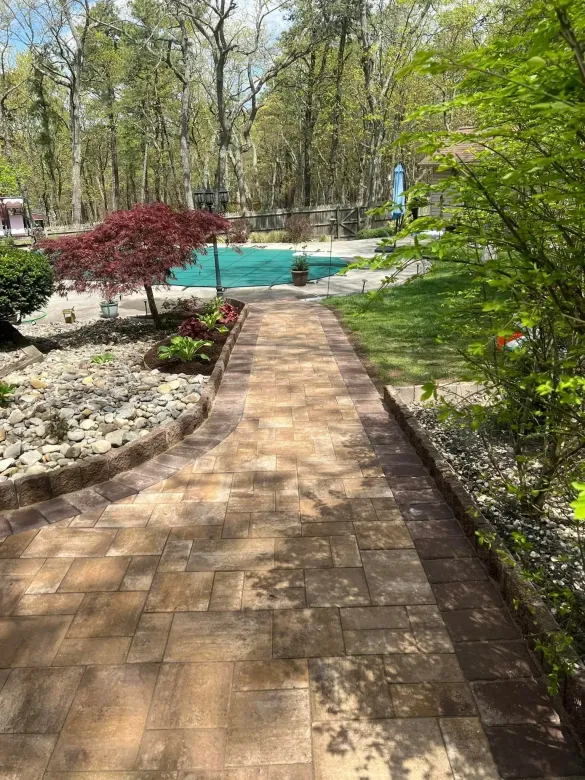 Stone path leads to a pool, surrounded by gardens and trees on a sunny day.