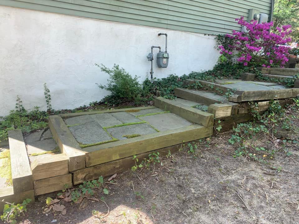 Stone steps with wood borders leading up to a house with a pink flowering bush.