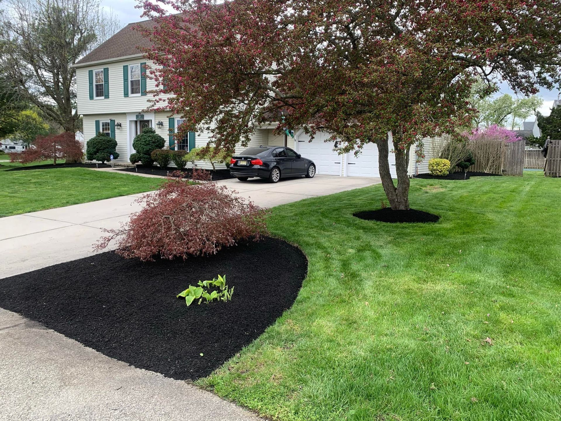 A house with a black car in the driveway, surrounded by freshly mulched landscaping and green grass.