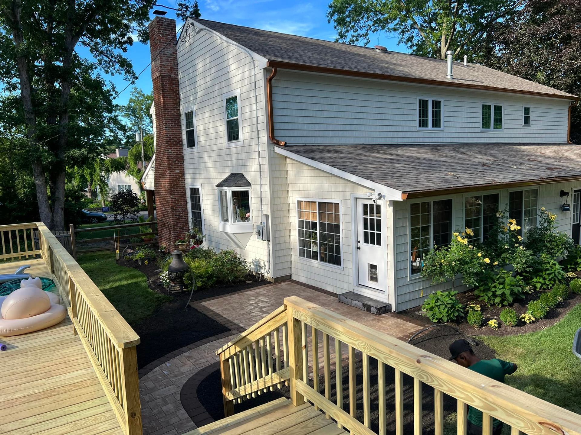 Two-story white house with a deck and brick chimney. A brick pathway leads to the entrance.