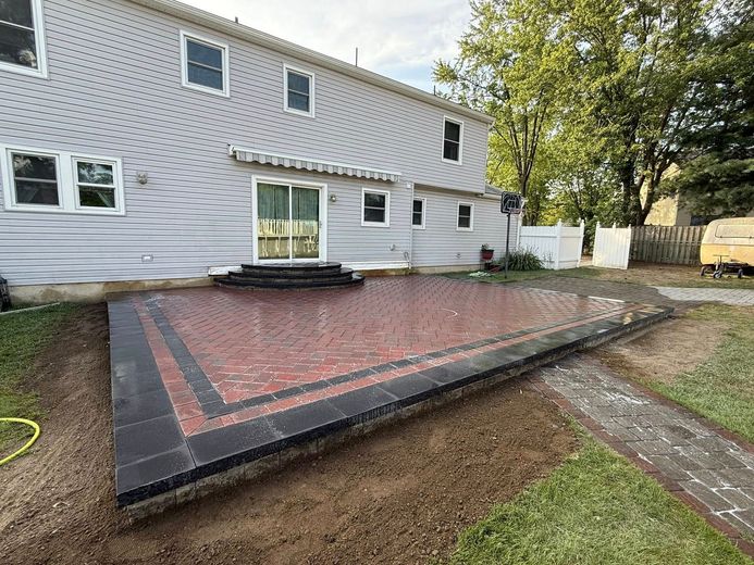 Backyard patio with red and black brickwork, next to a two-story house.