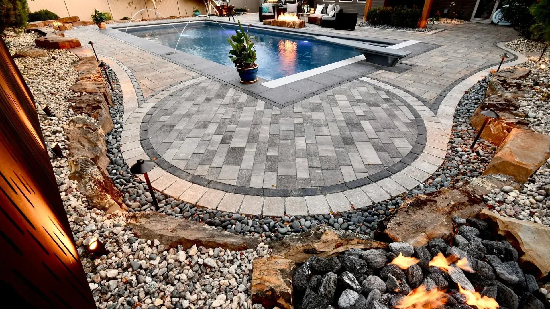 Backyard with pool and brick patio, rock features, and fire pit.