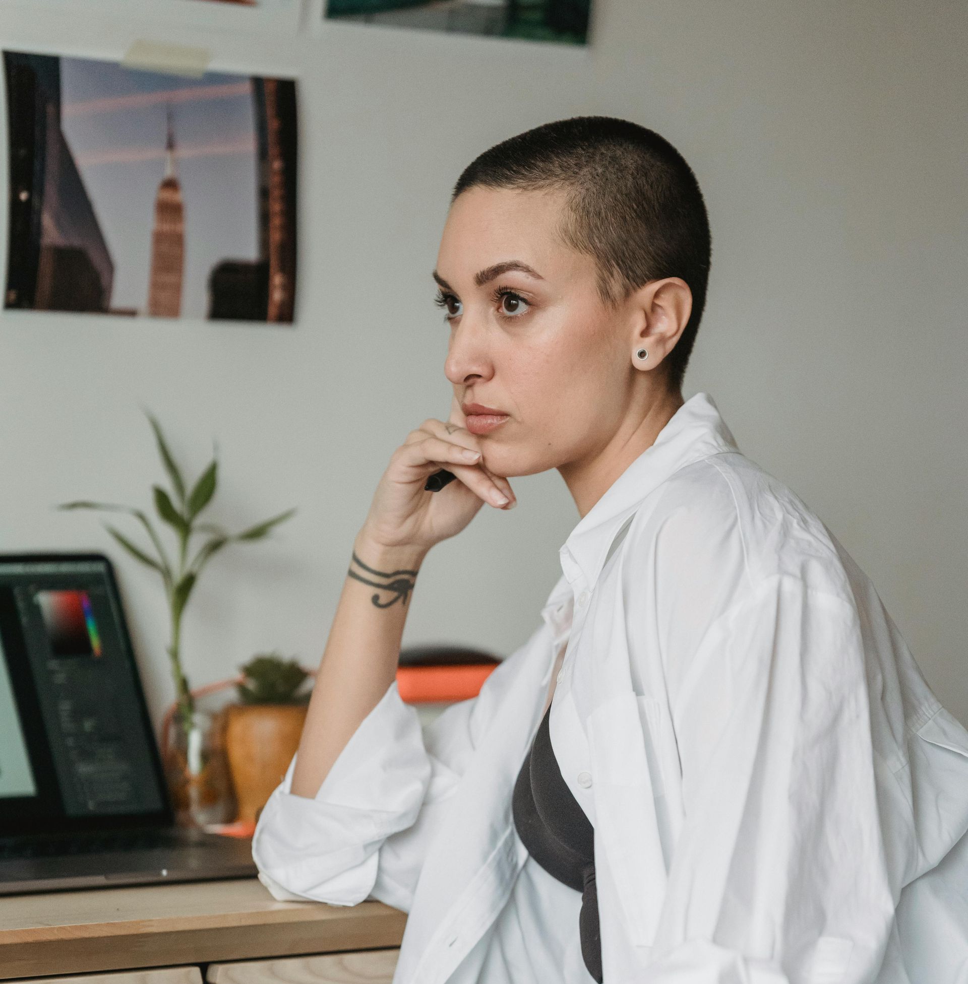 A woman with a shaved head is sitting in front of a laptop