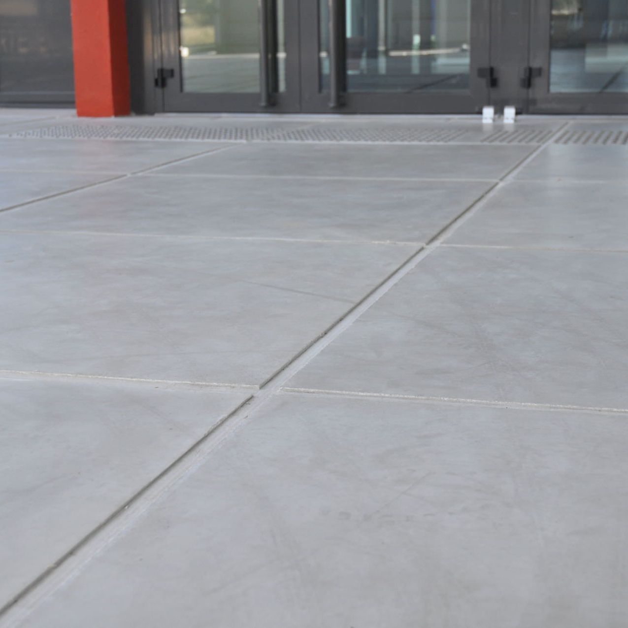 Gray concrete tiles leading to glass doors of a building.