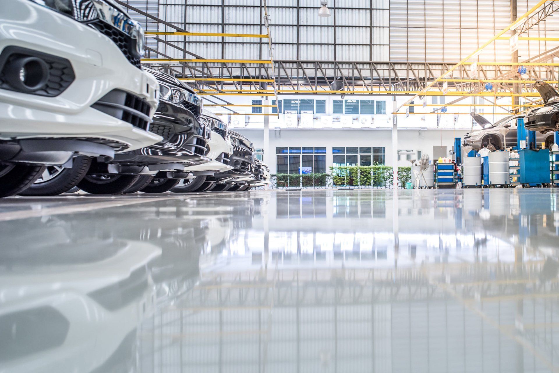 Row of cars parked inside a bright, industrial automotive workshop; shiny floor reflects the vehicles and building.