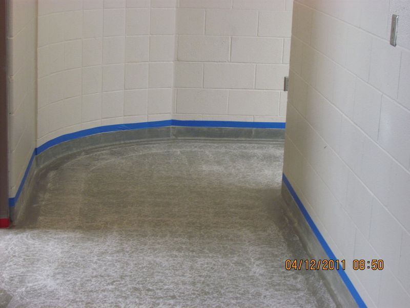 Hallway with gray floor, white walls, and blue tape along the baseboards.