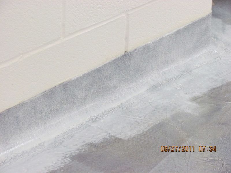 White painted wall and baseboard meets a gray floor with a white sealant.