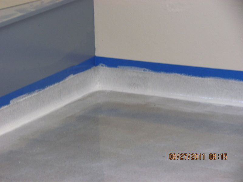 Blue painter's tape lines the corner where a gray painted floor meets white and blue walls.