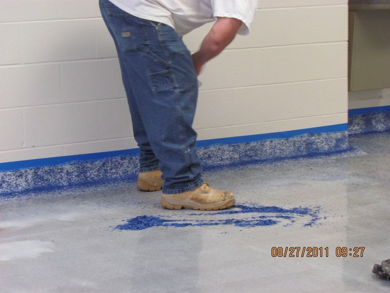 Person in jeans and work boots spreading blue flakes on a gray epoxy floor.