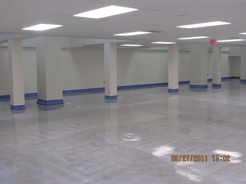 Empty, brightly lit room with white pillars, walls, and glossy gray floor; blue baseboards.