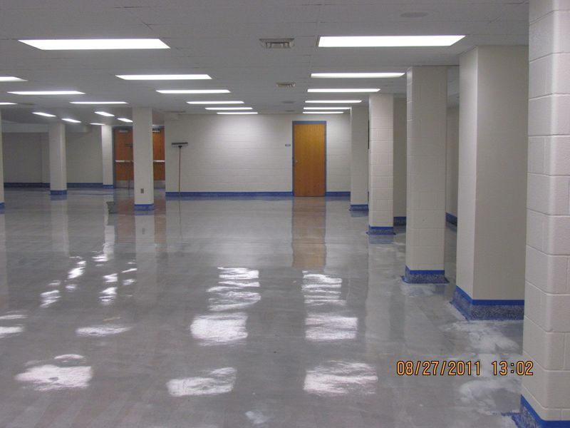 Empty room with glossy floor, rectangular lights, and support pillars. Doors line the white walls.