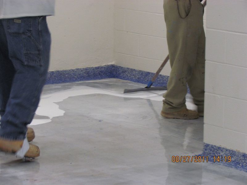 Two people applying a glossy coating to a floor with blue trim.