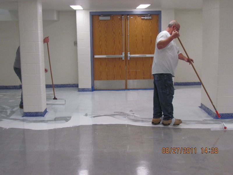 Two people applying sealant to a concrete floor in a hallway.