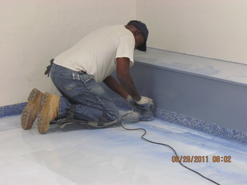 A person sanding a blue floor against a blue wall corner in a room.