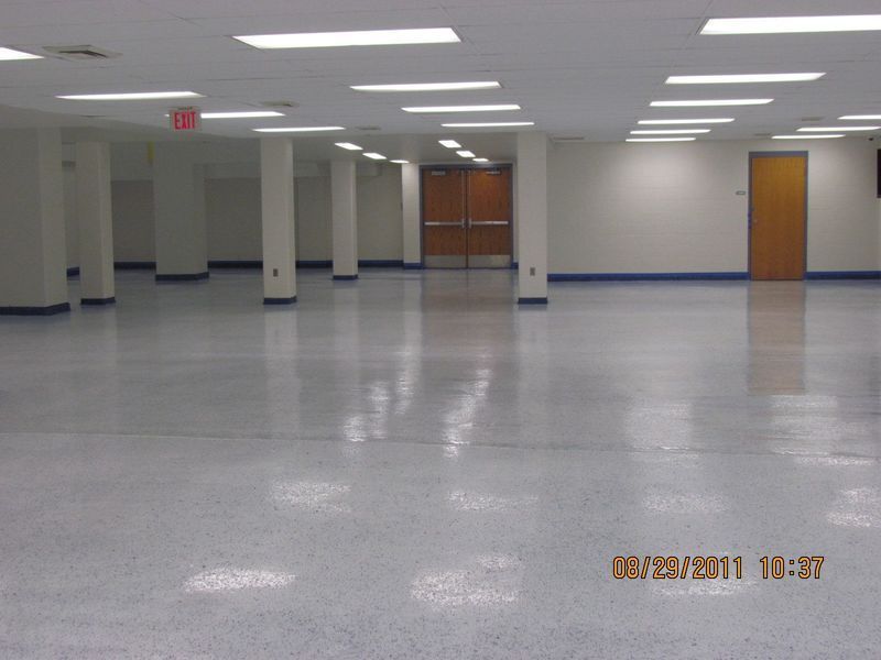 Empty, brightly lit room with a polished speckled floor, columns, and closed doors.