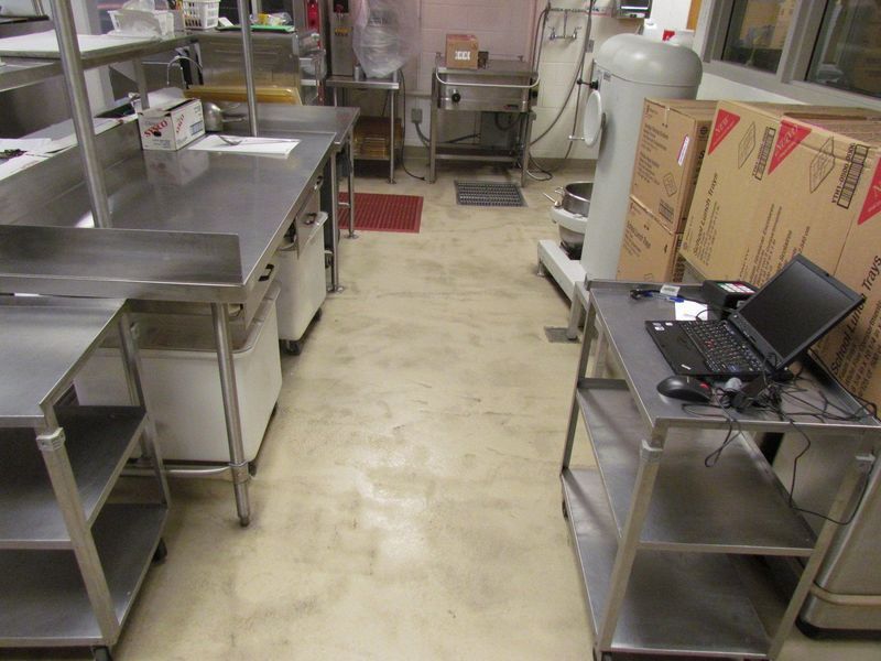 Commercial kitchen with stainless steel prep tables, shelving, and appliances; concrete floor.