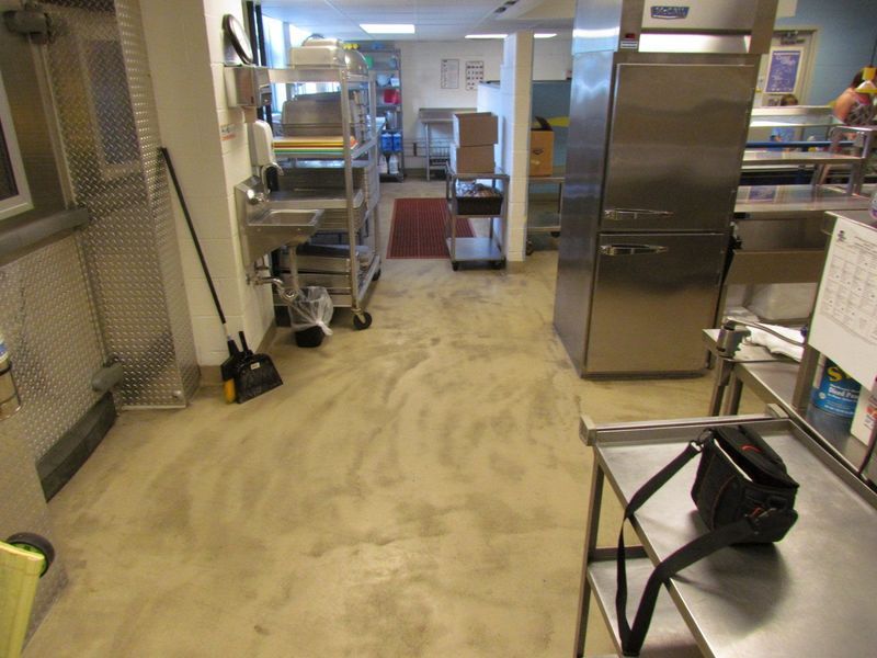 Commercial kitchen with stainless steel appliances, shelving, and tan flooring.