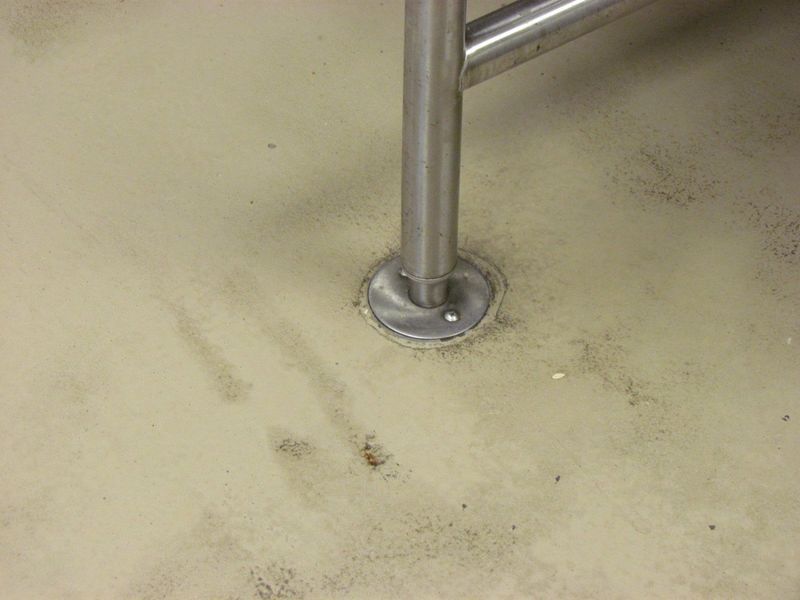 Stainless steel support post on a light-colored floor, showing wear and discoloration around its base.