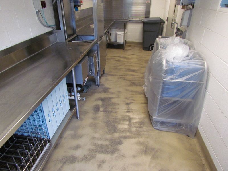 Kitchen with stainless steel counters, sink, dishwasher, and trash can; a cart with covered items.