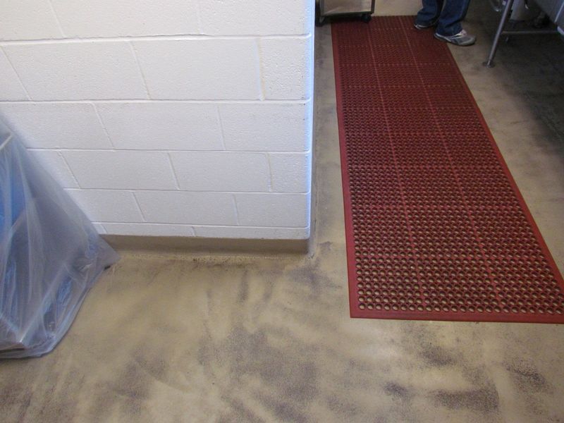 Red floor mat next to a white brick wall on a concrete floor. A person's legs are visible in the background.