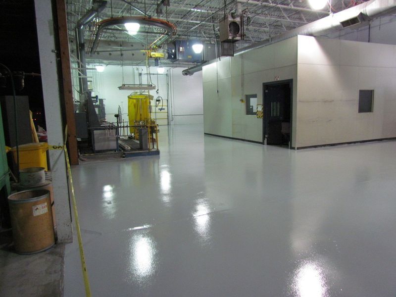 Spacious industrial room with shiny gray floor and a white enclosed area.