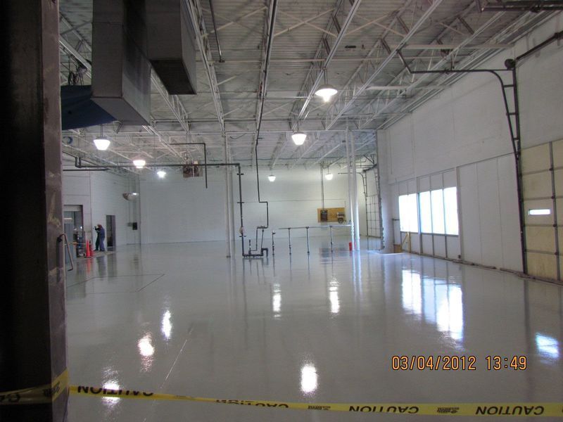 Empty, well-lit industrial warehouse with a shiny white floor and high ceiling. A large door is visible.