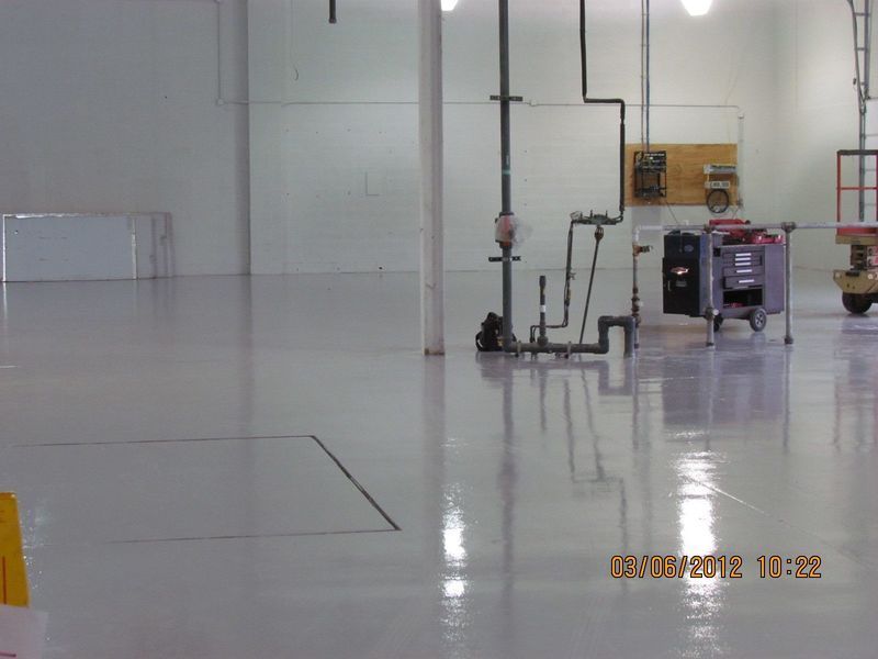 A freshly painted white industrial floor with plumbing and equipment visible.