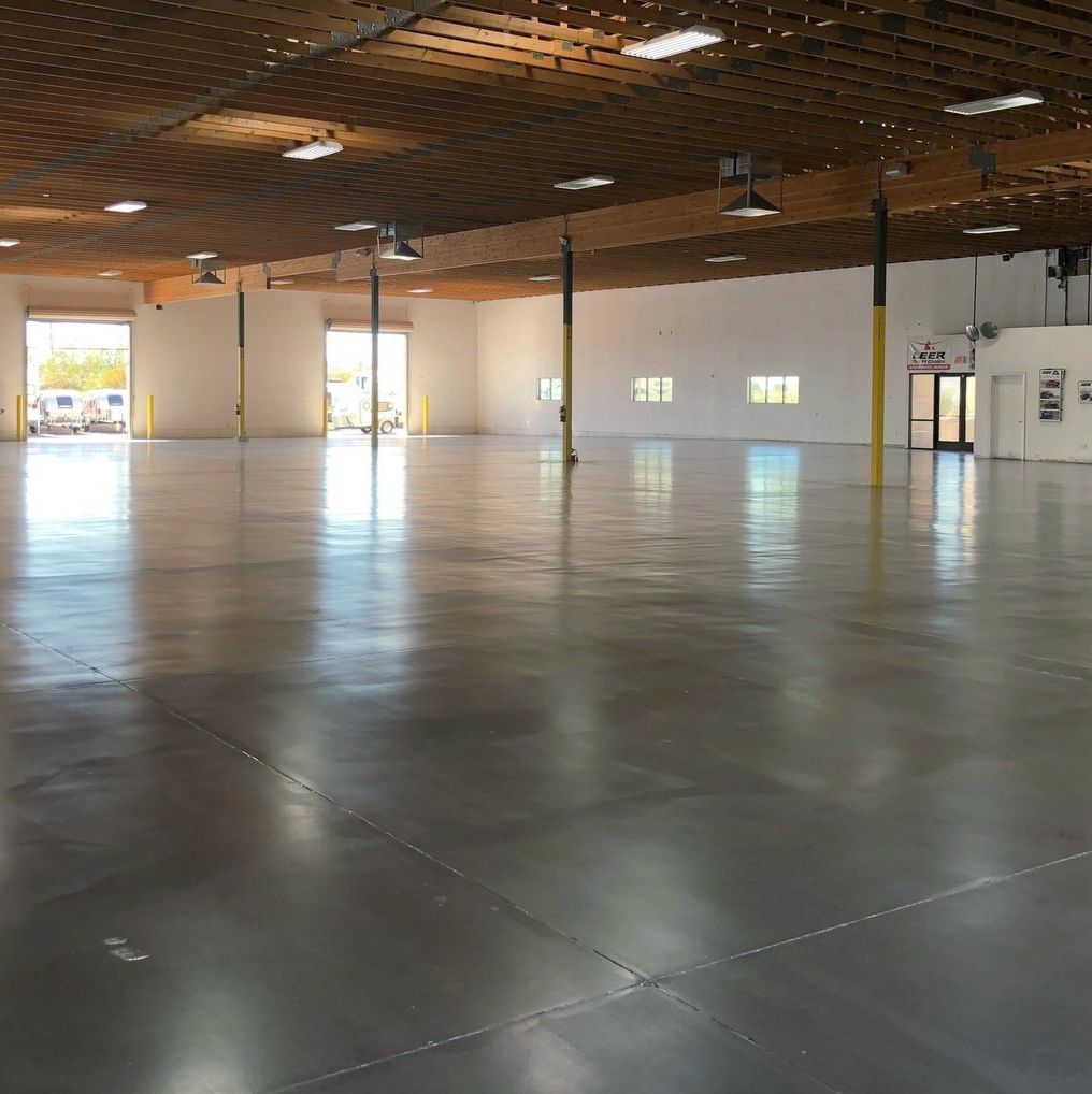 Empty warehouse with polished concrete floor, overhead lighting, and two open loading doors.