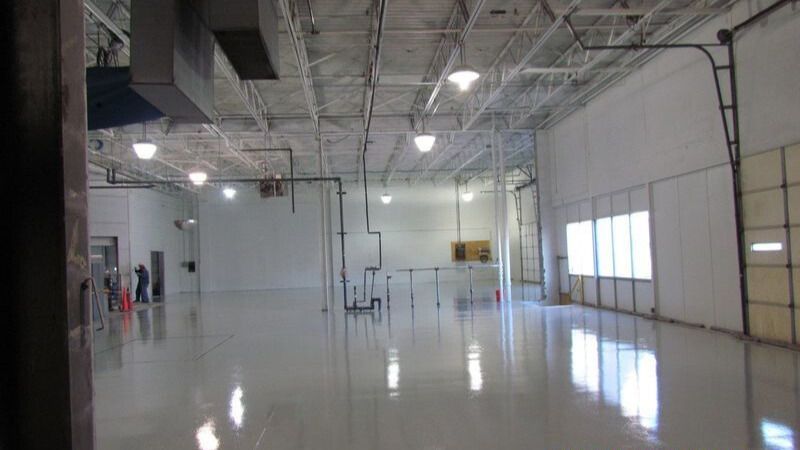 Interior of a large, empty, white-walled warehouse with a shiny floor.