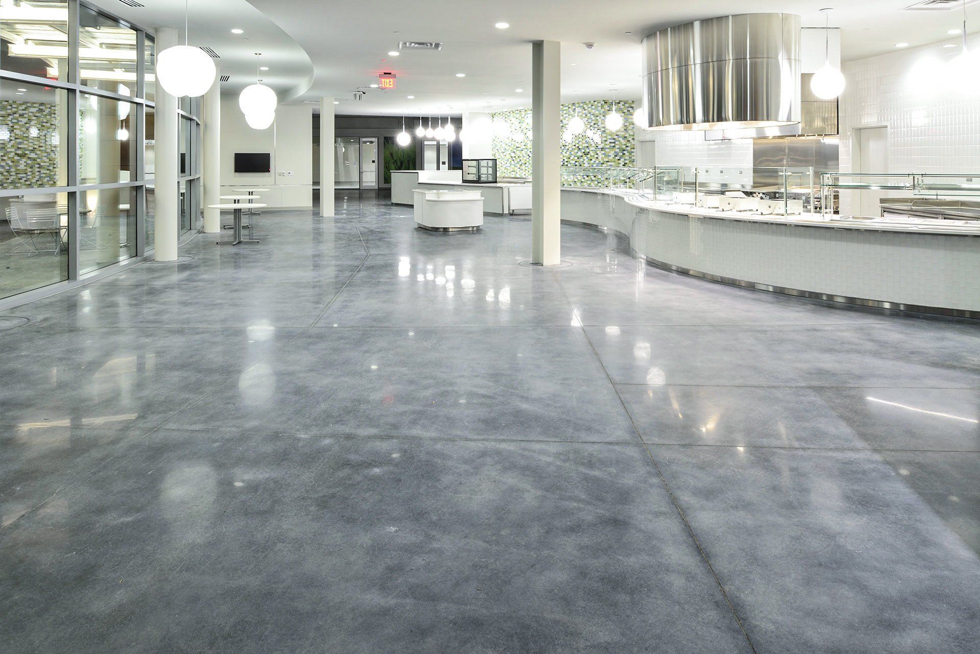 Polished concrete floor in a modern dining hall, with buffet counters and hanging lights.