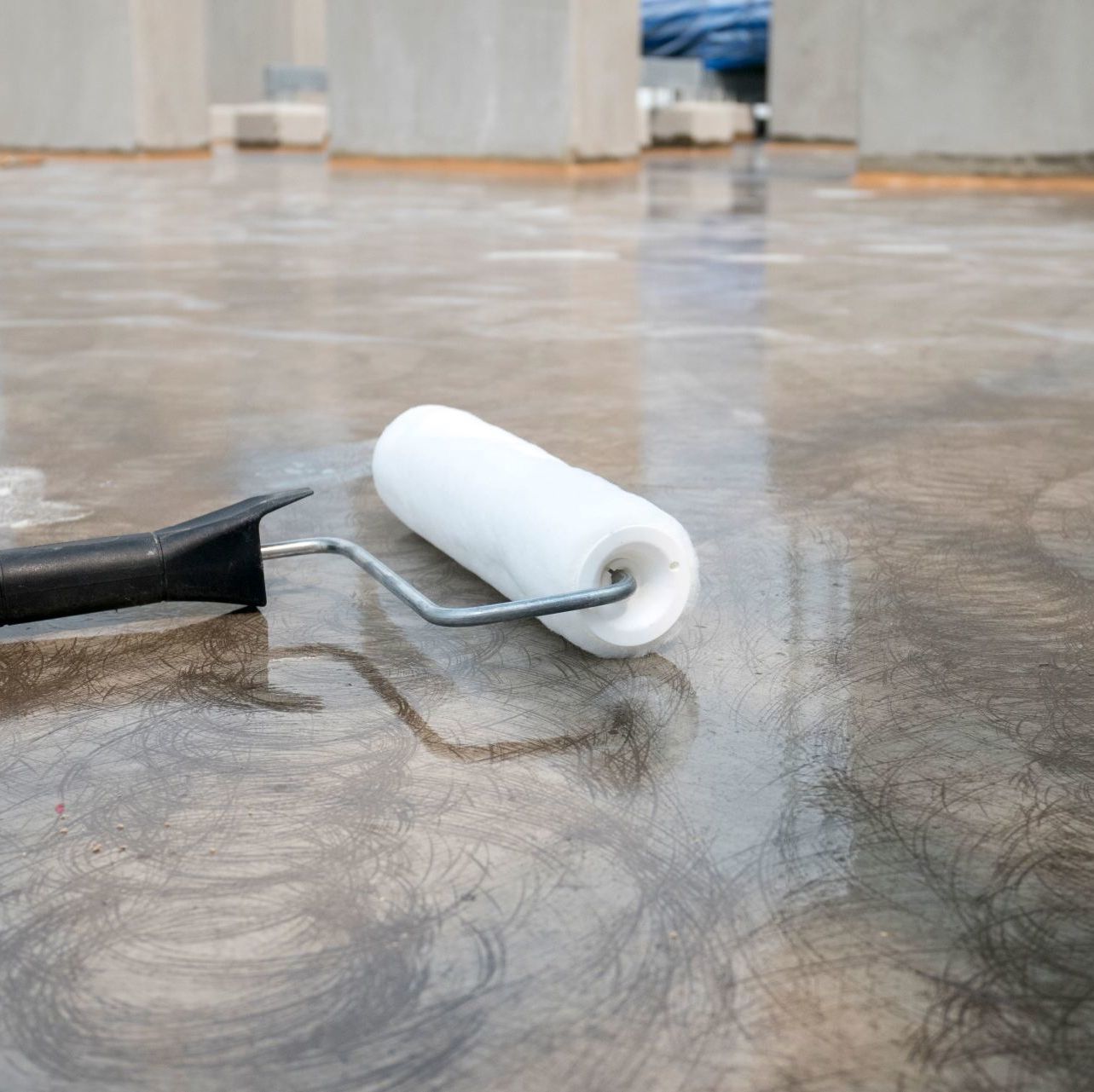 A paint roller on a wet, gray concrete floor; construction in progress.