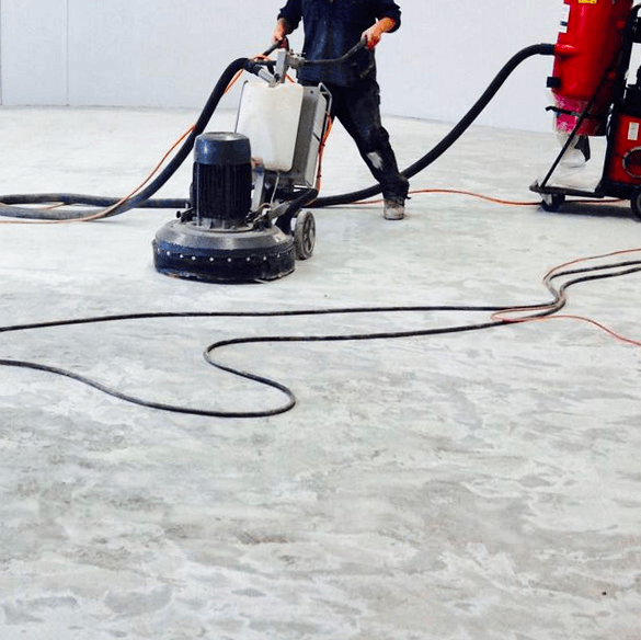 Person operating a floor grinder, attached to a vacuum, in a large, light-colored room.