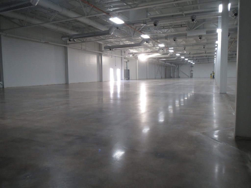 Large, empty warehouse with polished concrete floor reflecting overhead lights.