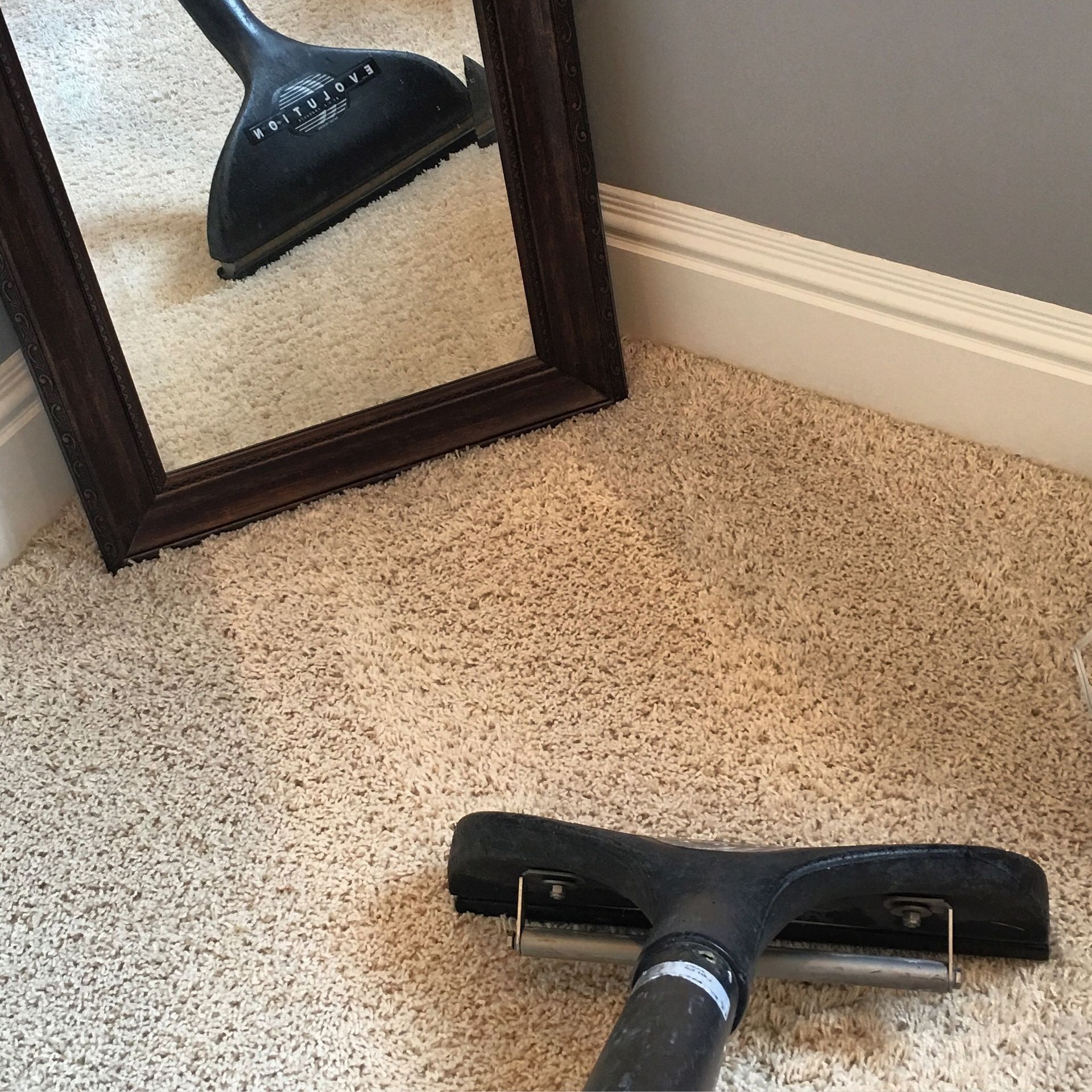 A vacuum cleaner is sitting on a carpet next to a mirror.
