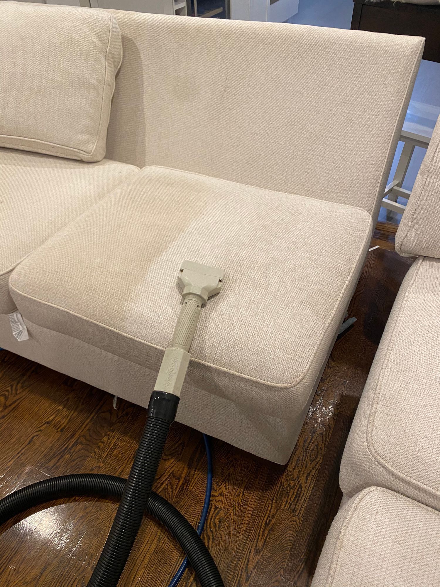 A vacuum cleaner is cleaning a white couch in a living room.