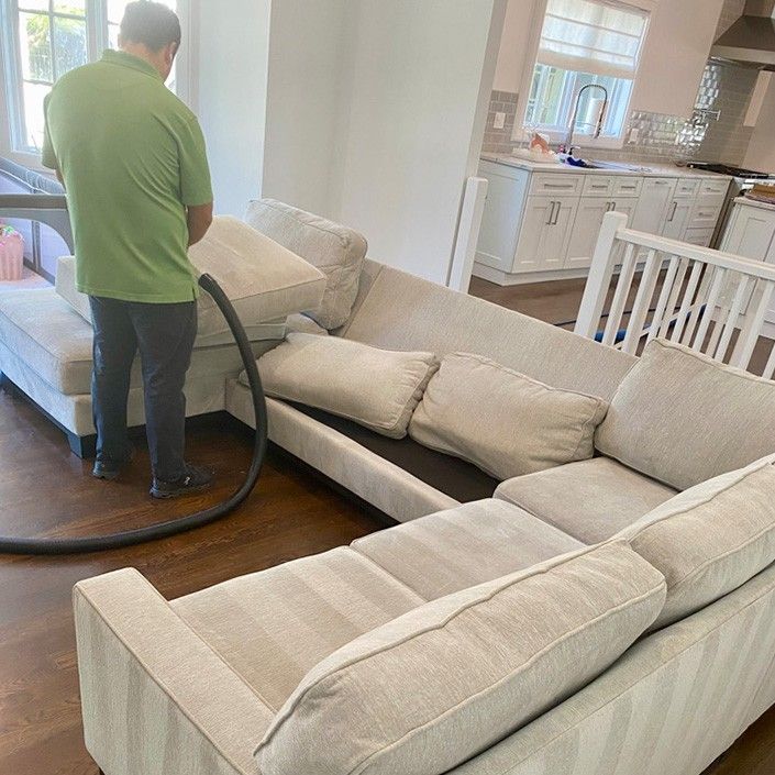 A man is vacuuming a couch in a living room.
