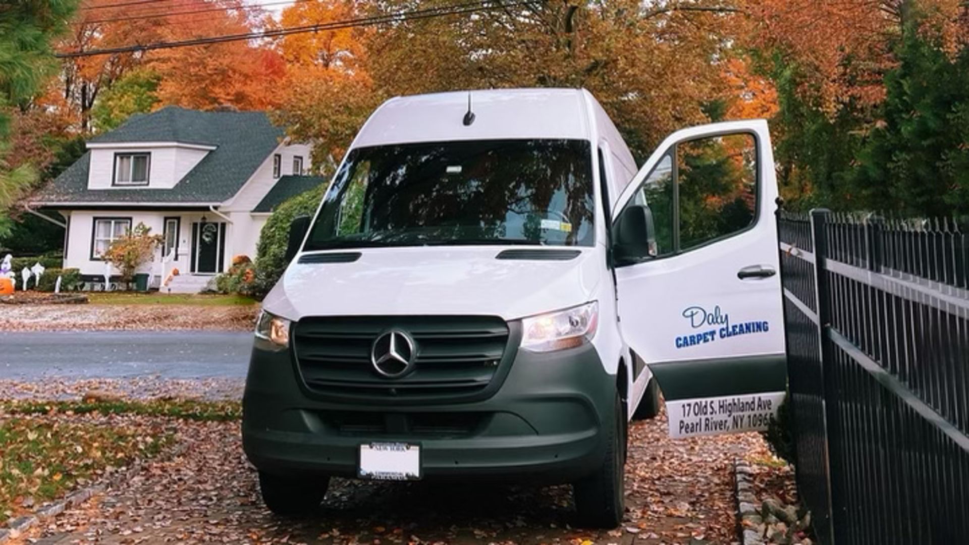 A white van is parked in front of a house with its doors open.