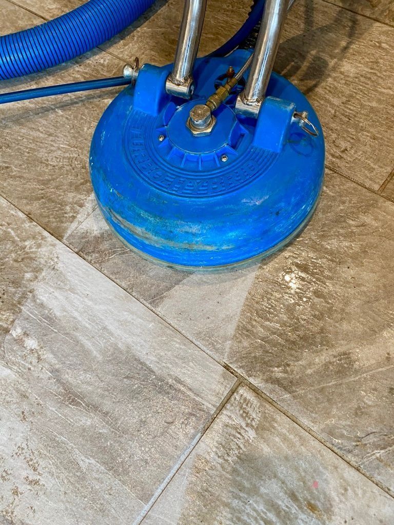 A blue vacuum cleaner is cleaning a tile floor.
